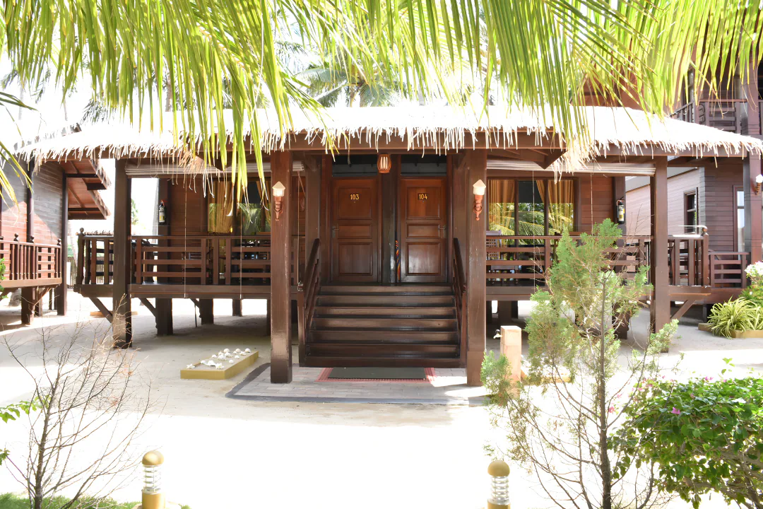 Two neighbouring rooms beneath one thatched roof, sharing a timber veranda with steps down to the sand, framed by palm fronds