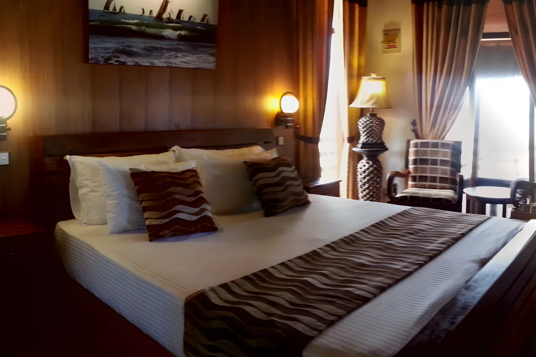 A large bed with wave-patterned cushions against timber-panelled walls, lit by warm wall lamps
