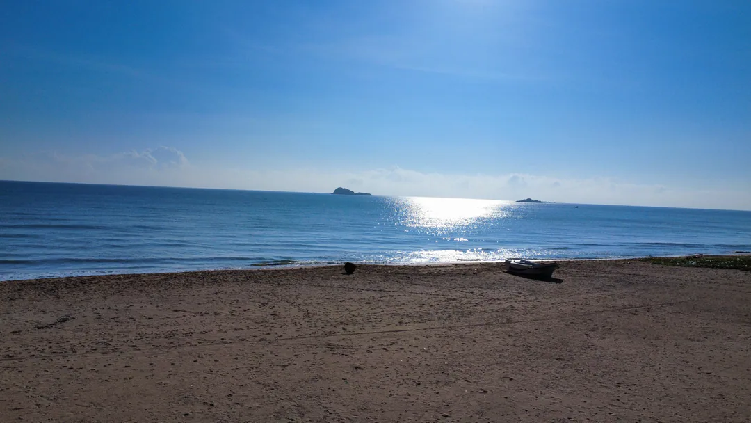 A boat drawn up on the empty beach, with sunlight on the sea and Pigeon Island offshore