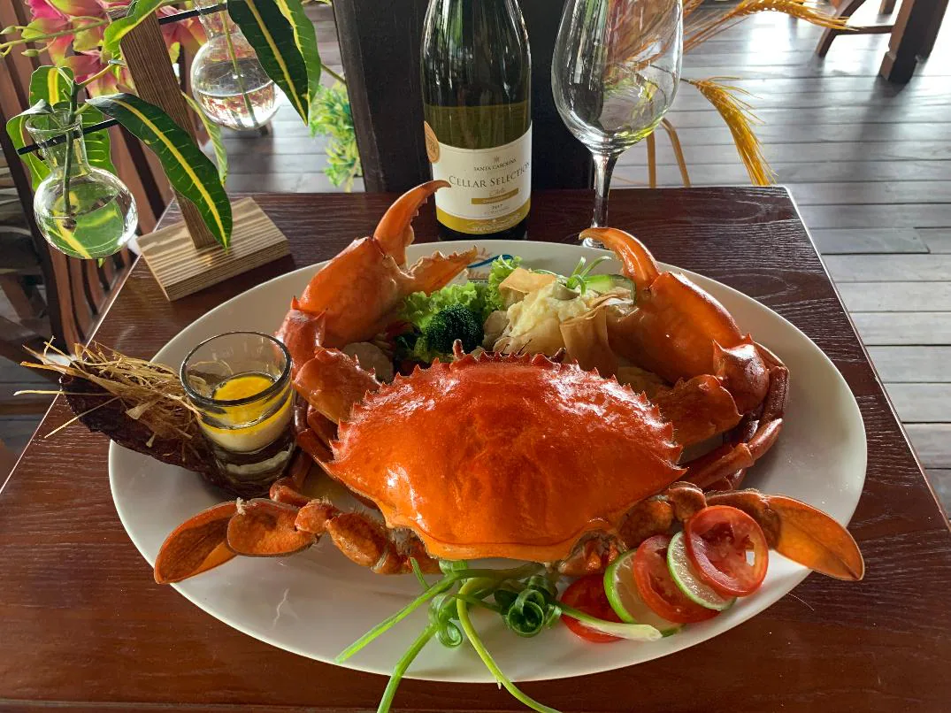 A whole crab served on a white plate with salad, beside a bottle of white wine and a glass
