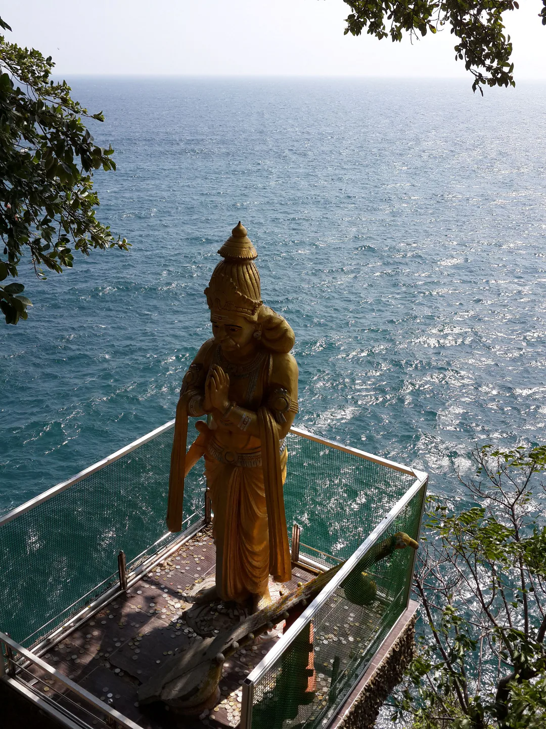 A golden statue with hands joined in prayer on a clifftop platform at Koneswaram, high above the sea