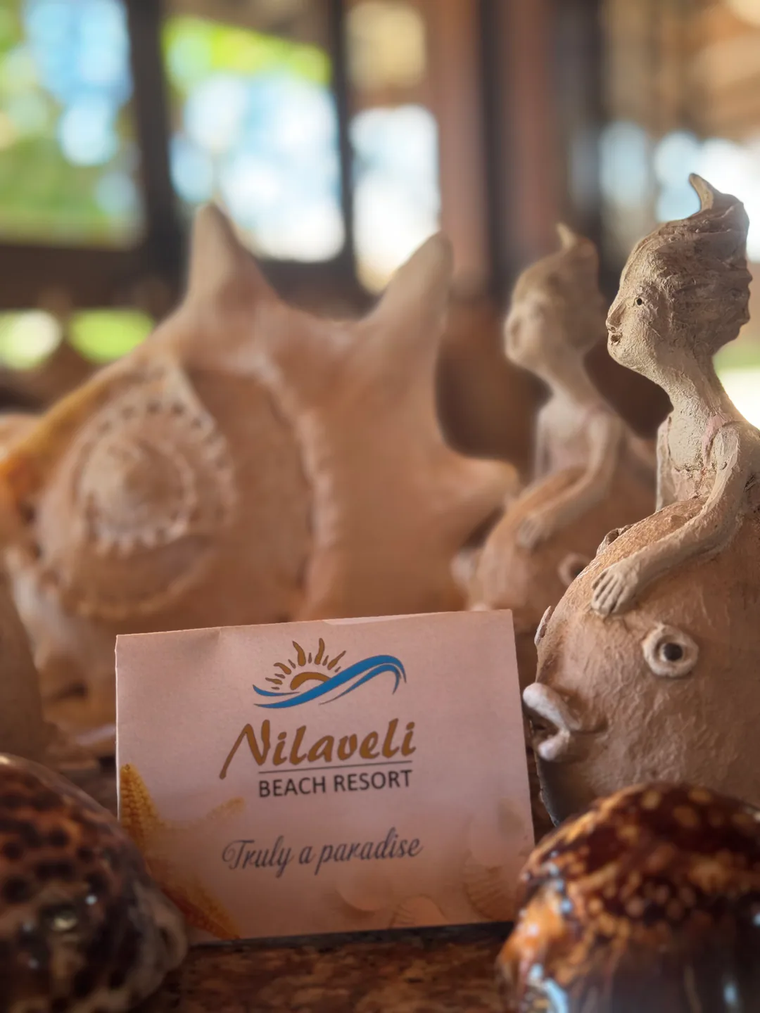 A Nilaveli Beach Resort card reading “Truly a paradise” among clay figures and shells