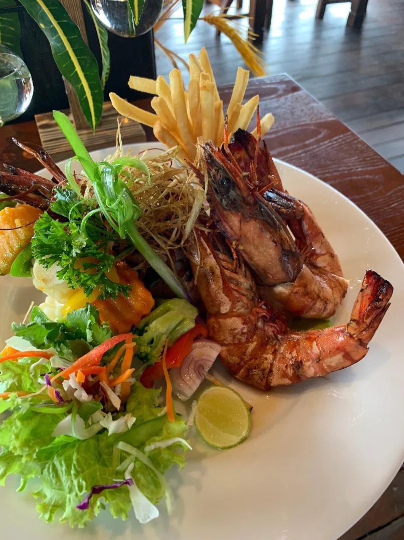 Grilled king prawns with salad and crisp fries on a white plate