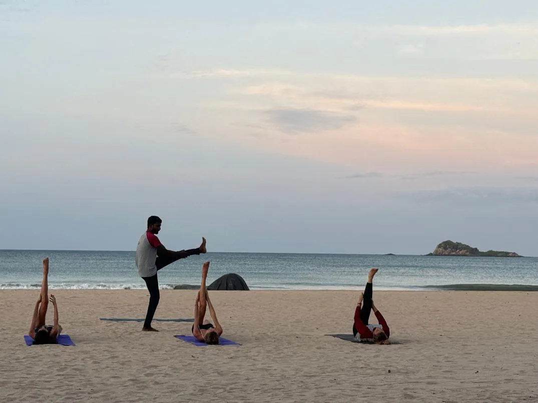 A yoga teacher leading guests through stretches on mats on the beach at dusk, with Pigeon Island offshore