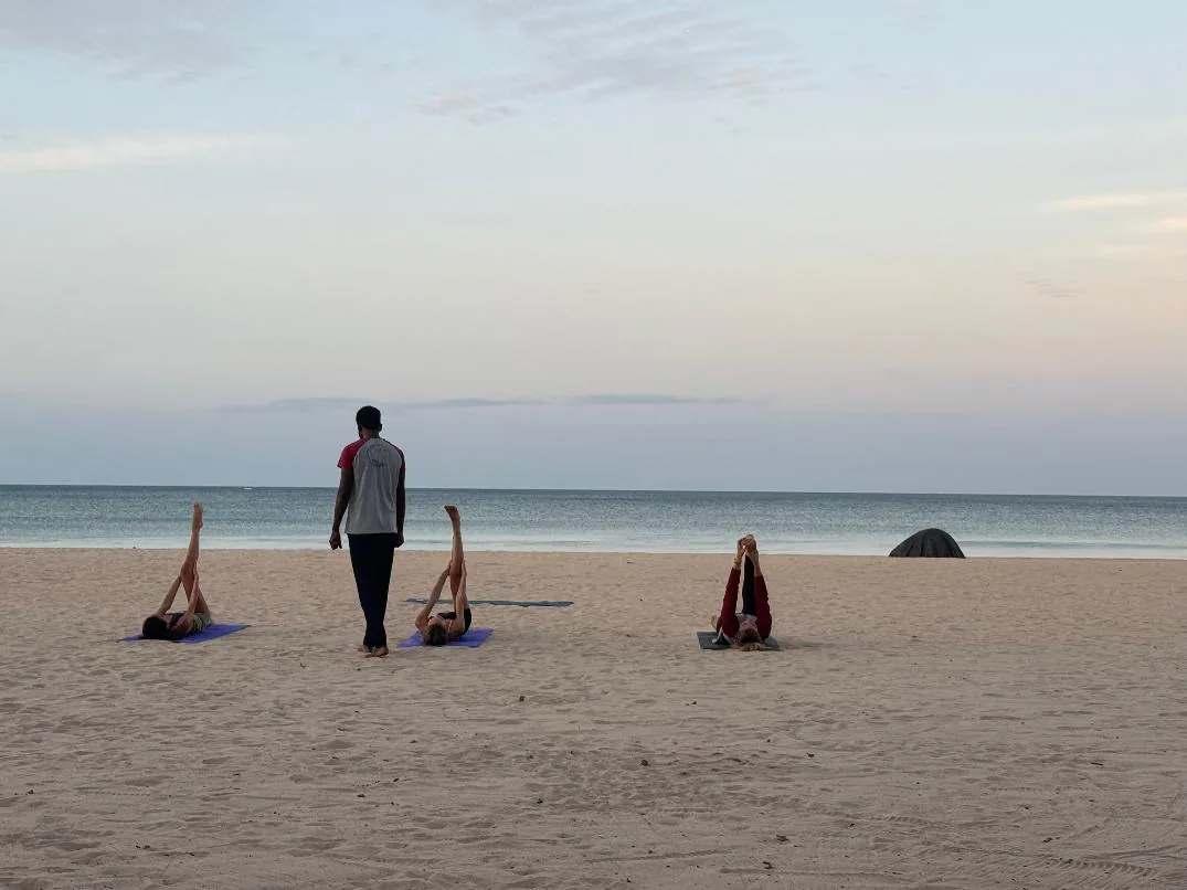 Guests on yoga mats on the sand at dusk as their teacher walks between them