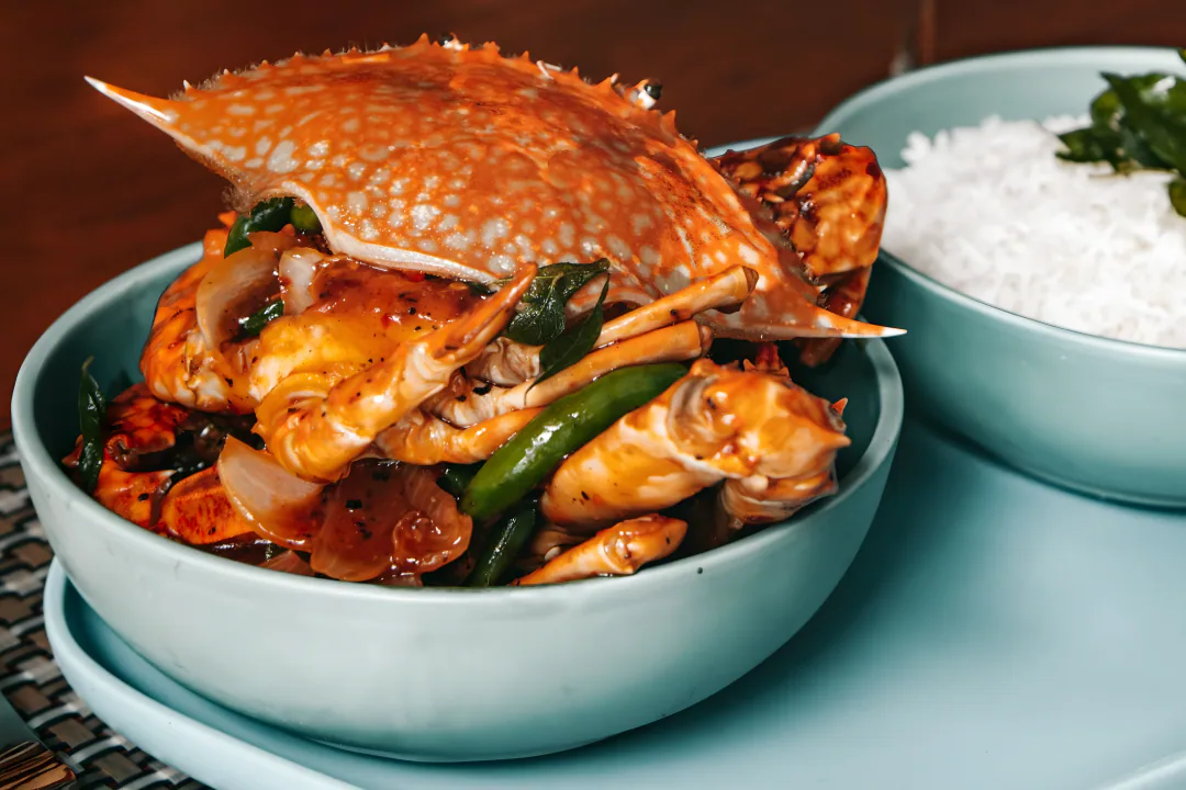 A spiced crab dish with green beans and onion, beside a bowl of rice