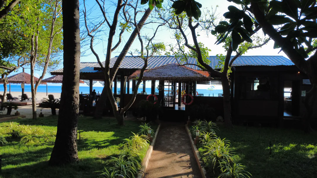 A garden path leading to the timber restaurant pavilion, with tables inside and the sea beyond