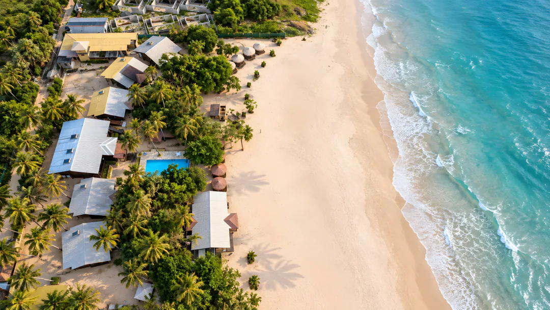 The resort from above: cabanas and the pool among palms beside the beach