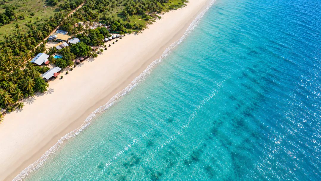 The resort from offshore: cabanas, the pool and palms along a long white beach and turquoise sea