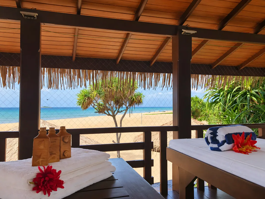 Massage beds with folded towels and flowers in the open-sided timber spa pavilion overlooking the beach